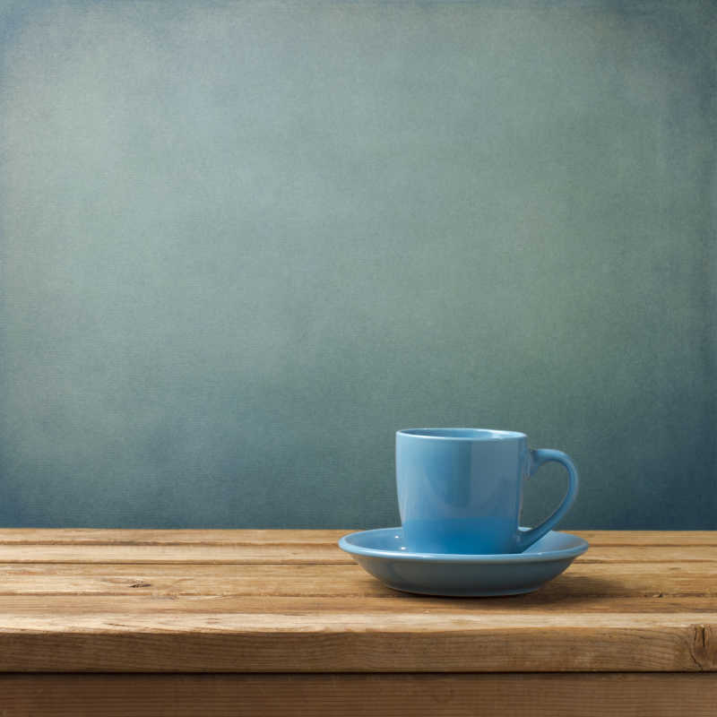 蓝色的咖啡杯在木制的桌子上浅蓝色背景