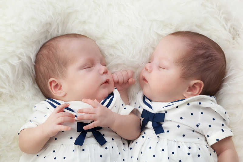 新生双胞胎姐妹睡在白色的毛皮上穿着水手服