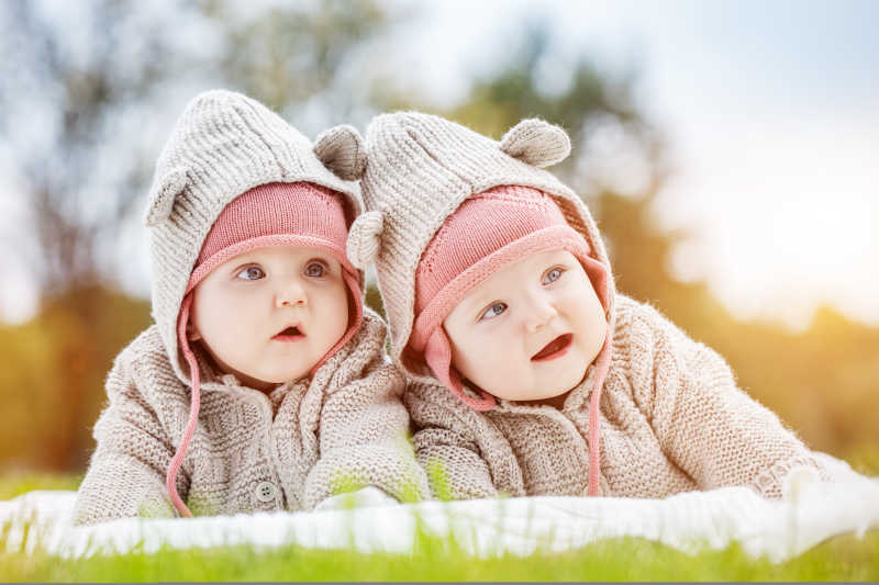 穿着舒适的毛衣的可爱的双胞胎宝宝趴在公园草地里