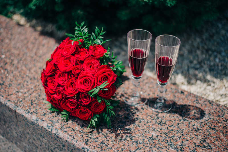 鲜红玫瑰捧花和两只红酒杯