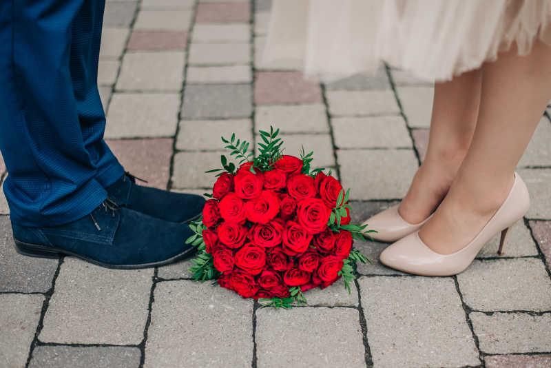 新婚夫妇的脚和红色玫瑰捧花特写
