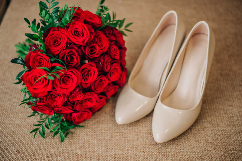 棕色背景上的红玫瑰捧花和米色高跟鞋