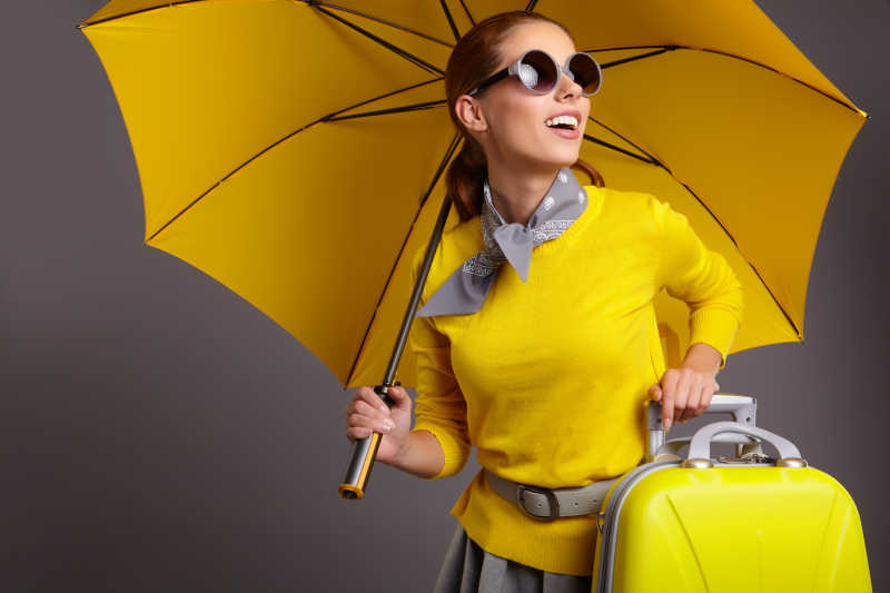 带着黄色的手提箱黄色伞的美丽女人