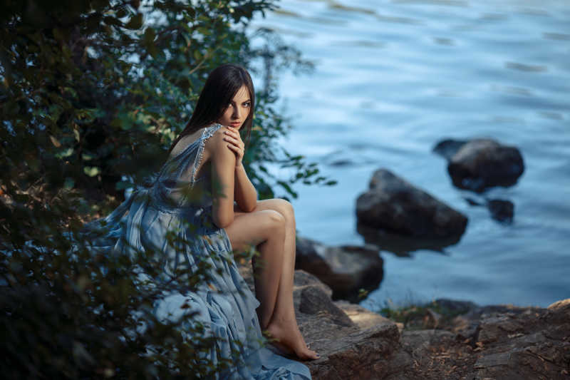坐在河边岩石树木旁边的女模特