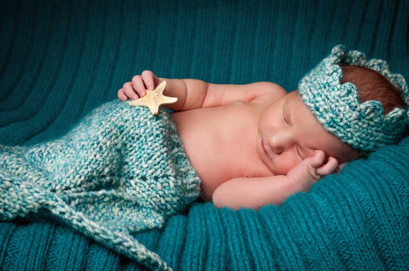 绿色针织背景下穿着针织鱼尾的睡着的小婴儿