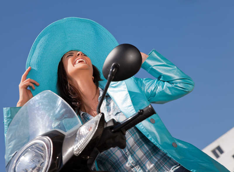 坐在摩托车上的戴着帽子的大笑女性