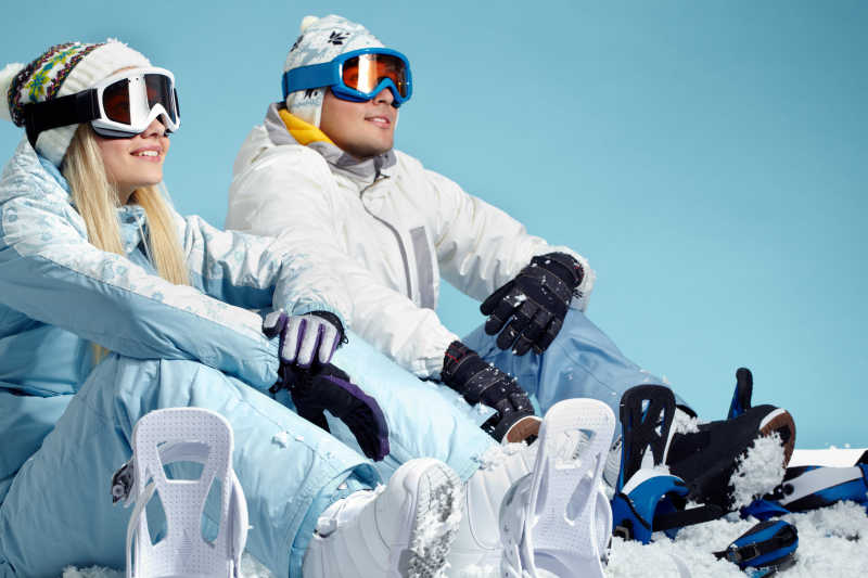 年轻的两个人穿着运动衣戴着滑雪镜坐着休息