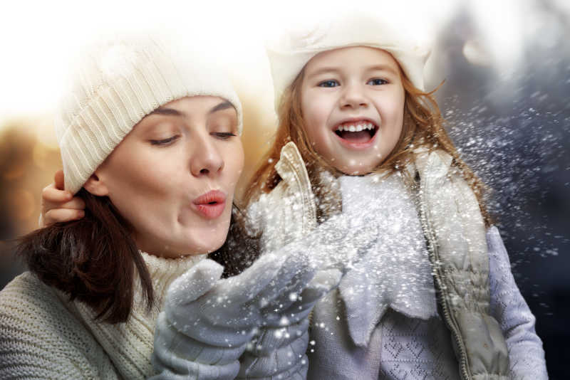 下雪天妈妈吹着手里的雪女儿开心的笑着