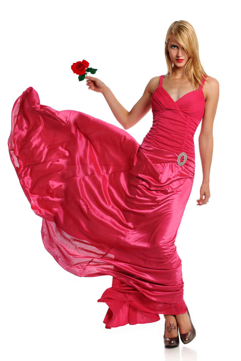 穿着玫红色丝绸礼服拿着一朵玫瑰花的年轻性感女模特