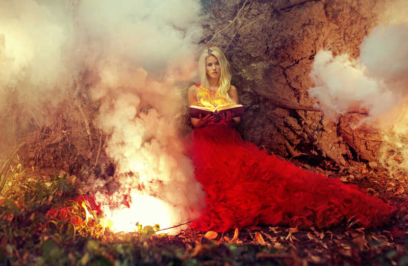金发美女穿着红色衫裙坐在大树下手捧魔法书