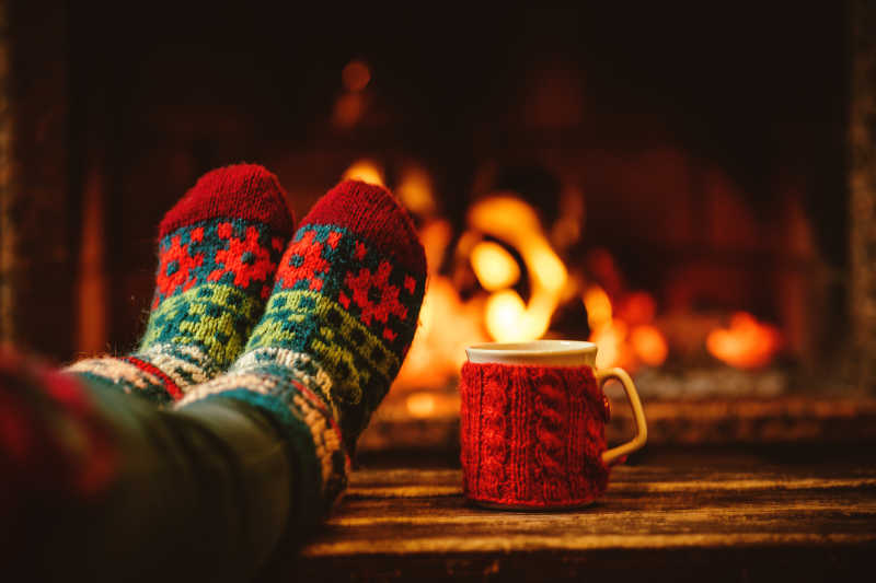圣诞壁炉旁的羊毛袜脚和一杯热饮料
