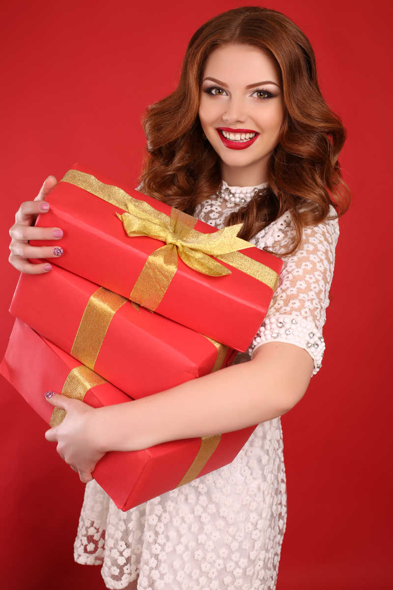 红色背景上抱着圣诞礼物盒的快乐女性