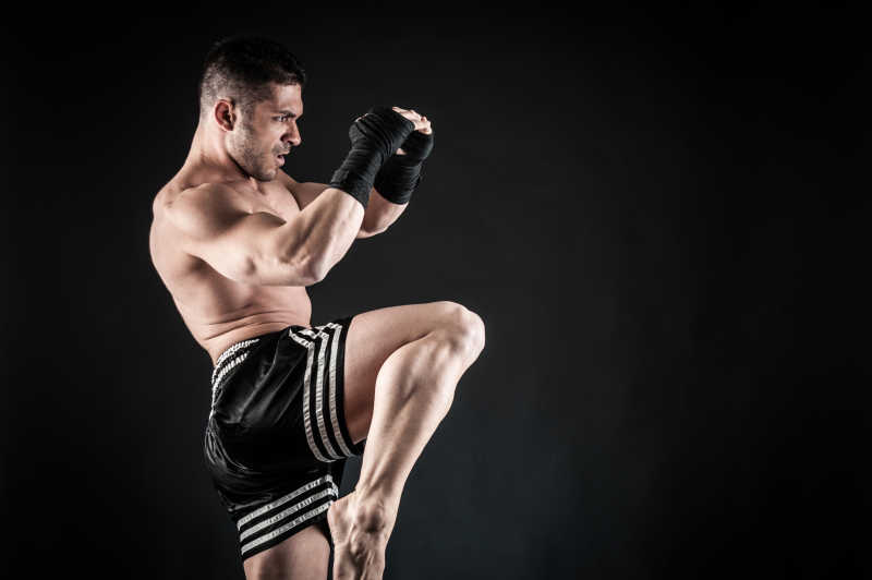 黑色背景上的拳击运动员练习侧踢