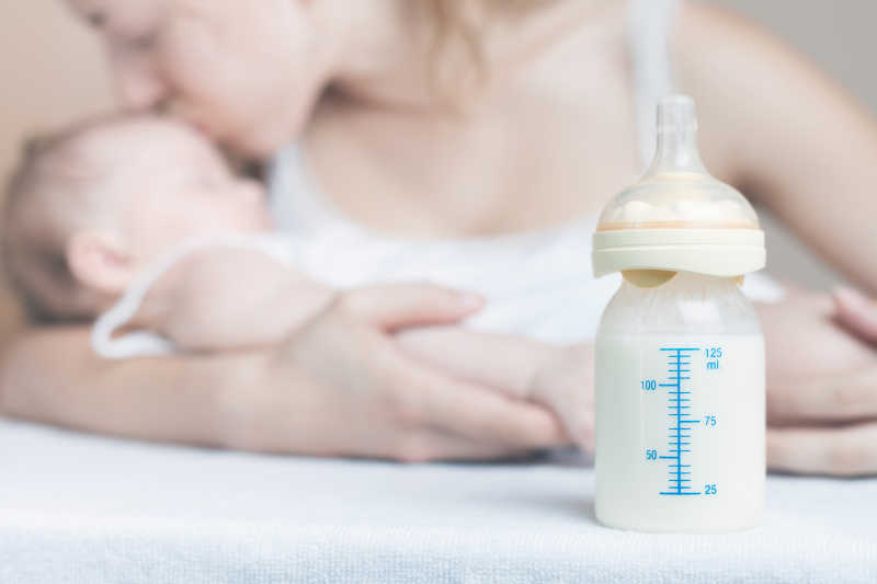 母亲亲吻婴儿的背景下的奶瓶特写