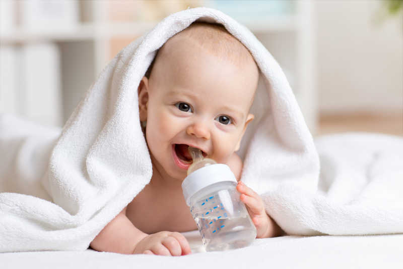 盖着毛巾趴着的拿着奶瓶喝水的婴儿