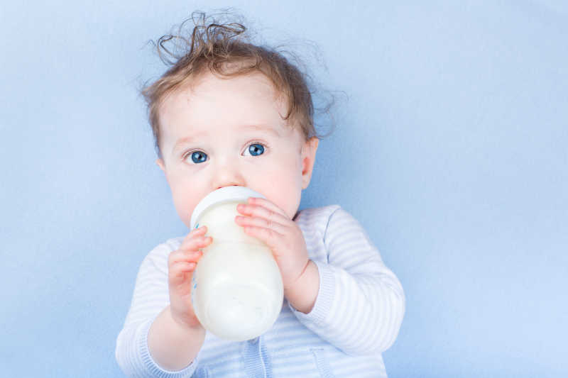 有一双漂亮的蓝眼睛的小宝宝拿着奶瓶和奶粉