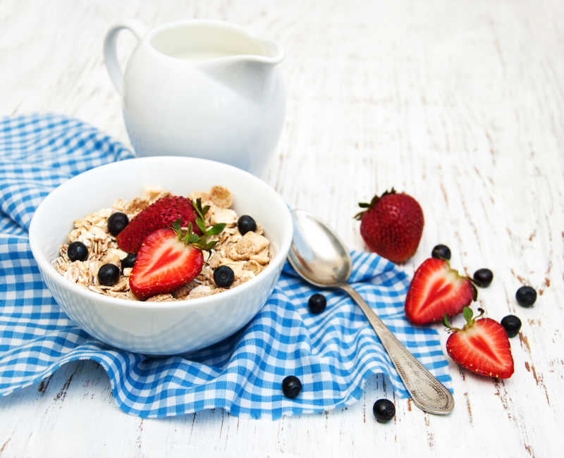 木质背景上的蓝色格子布铁勺草莓浆果牛奶和什锦麦片早餐