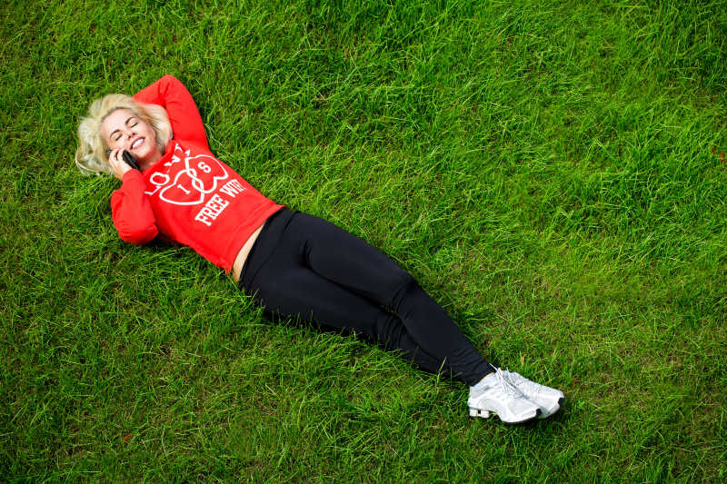 闲暇时刻躺在草地上打电话的年轻女子