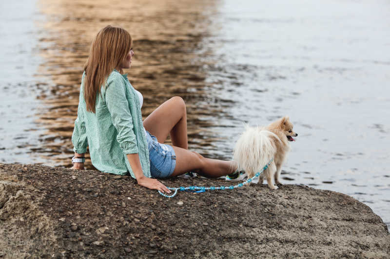 闲暇的女子牵着宠物狗坐在河边