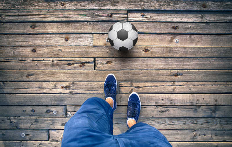 在旧木地板上的人腿和足球