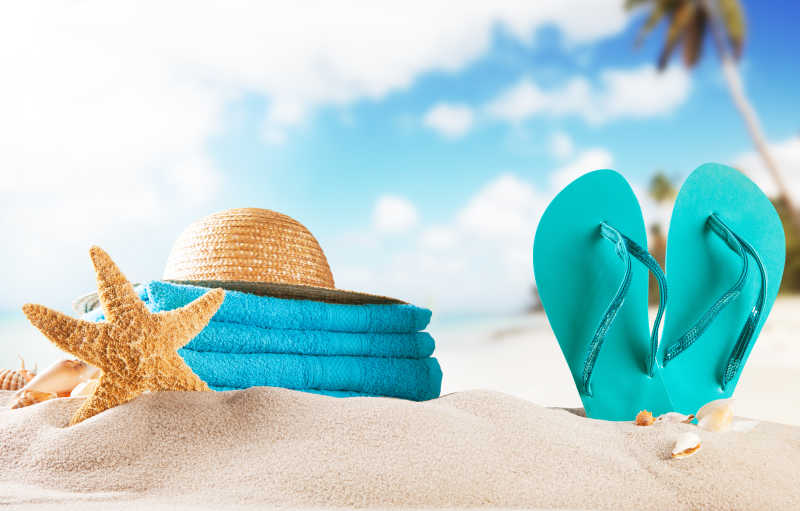 在夏日的海滩有一双蓝色凉鞋帽子和毛巾