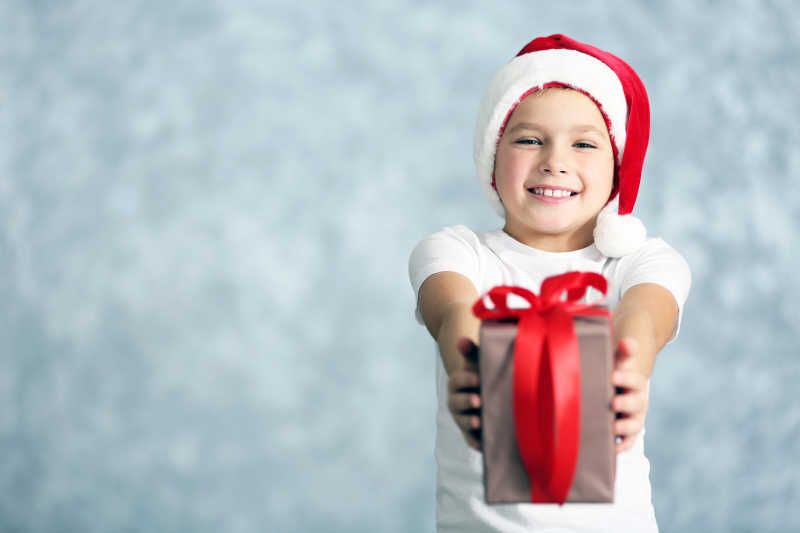 戴圣诞帽的男孩拿着红色丝带礼品盒