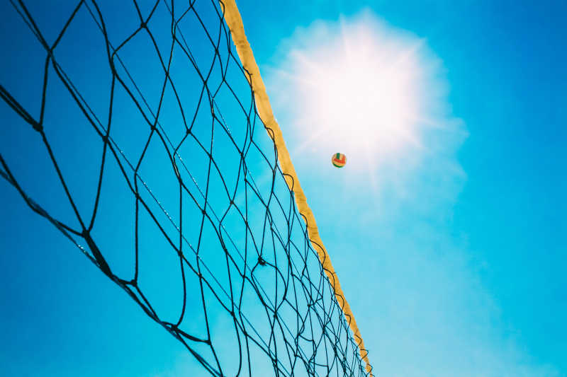 艳阳蓝天下的排球网和飞起来的排球