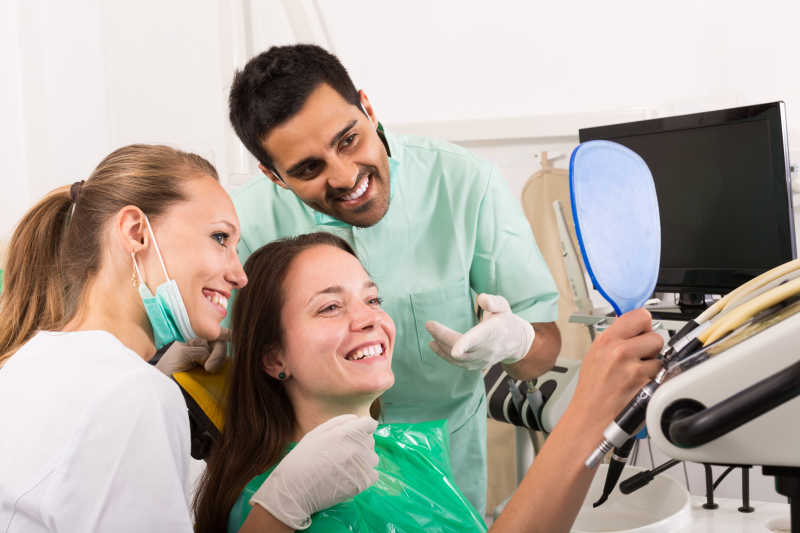 牙科医生与助理和病人一起用镜子看着医治好的牙齿