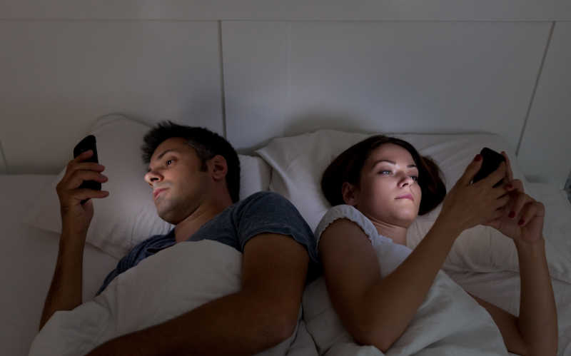 睡觉前看着手机的夫妇