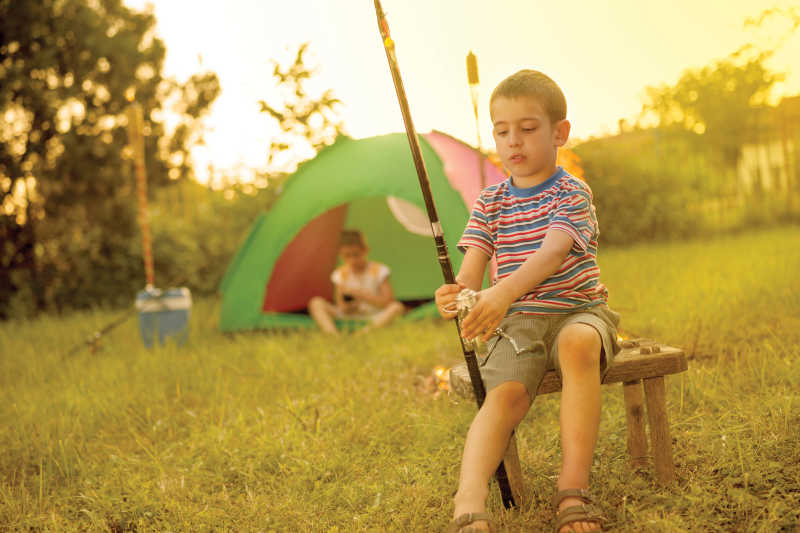 露营中学习使用钓鱼竿的小男孩