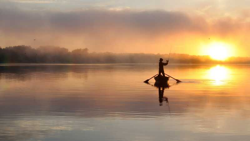 日落晚霞下的湖面上的钓鱼爱好者的特写