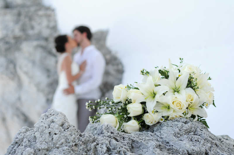 岩石上的白色花朵和新郎新娘接吻