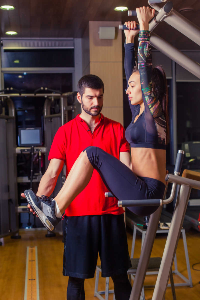 私人教练帮助女子腹部肌肉锻炼按单杠