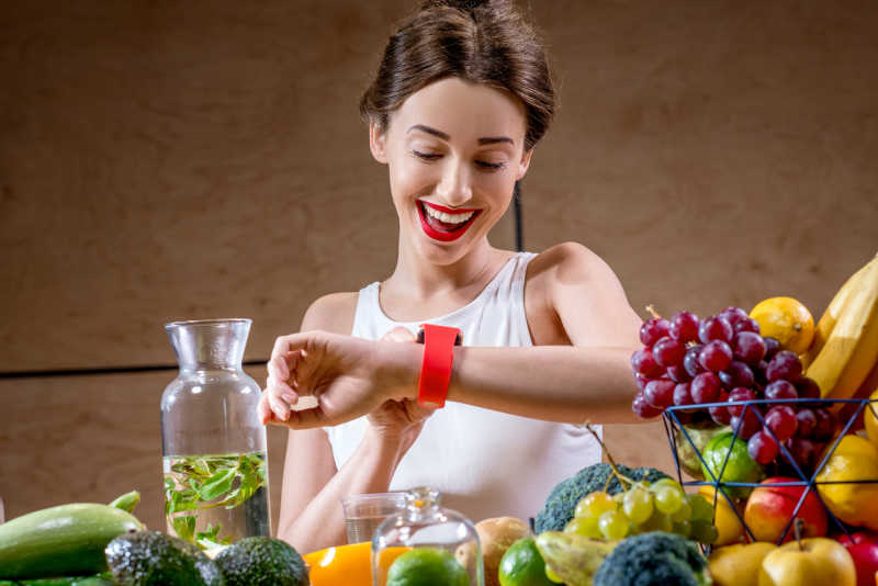 年轻漂亮的女人在桌旁看着手表水果和蔬菜