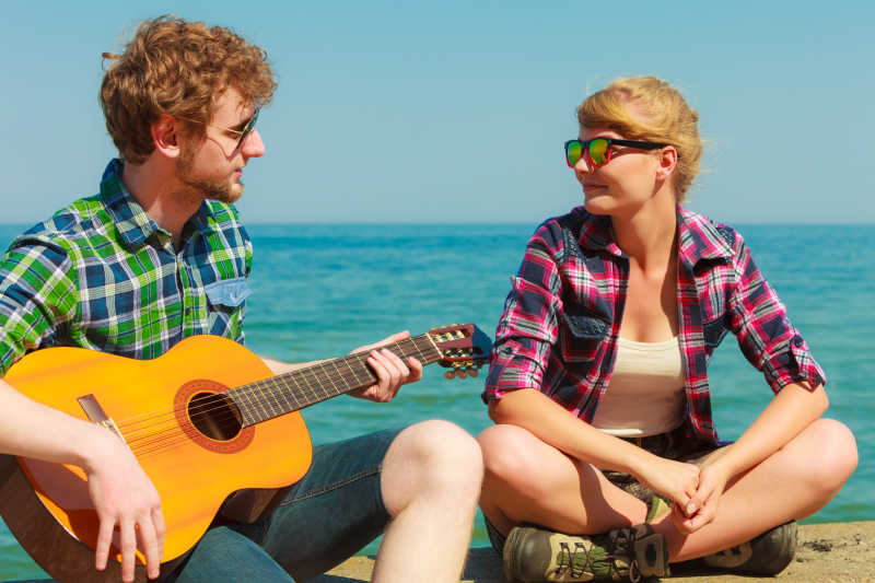 在海边给女朋友弹吉他的年轻人