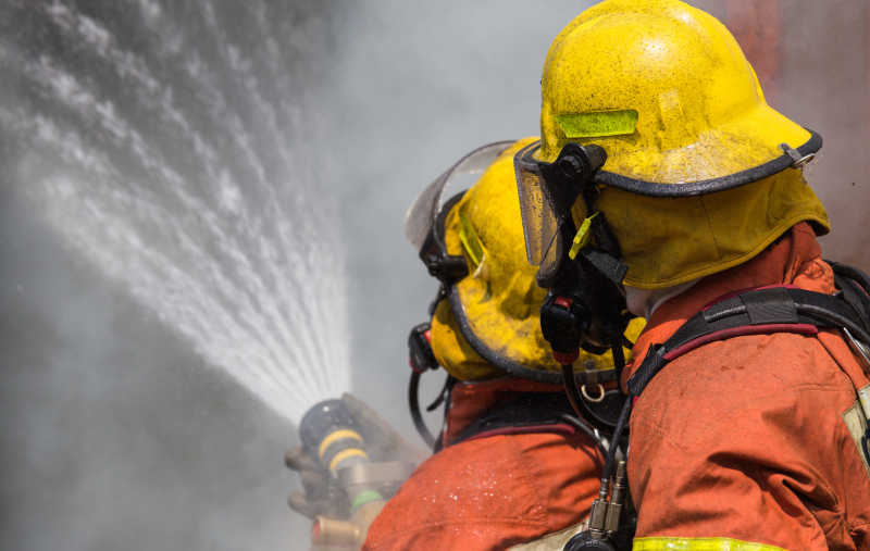 两名消防员戴着头盔和氧气面罩喷水灭火