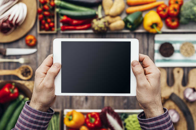 手握数码触摸屏片和健康的蔬菜