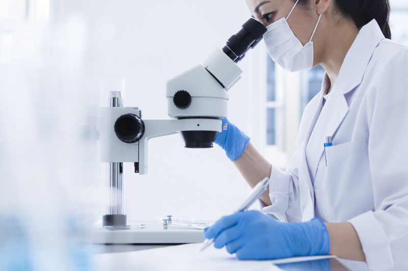 女性研究人员通过显微镜观察记笔记