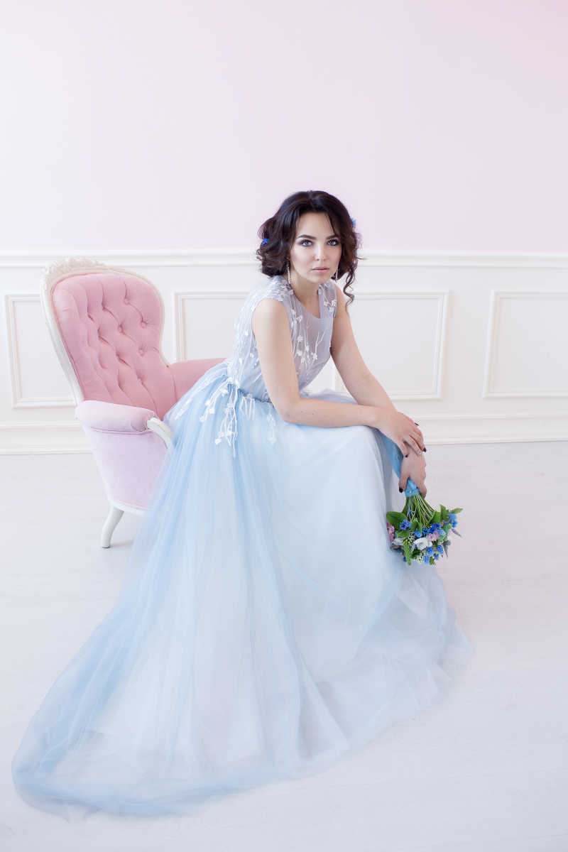 在粉色椅子上坐着的穿蓝色婚纱的新娘