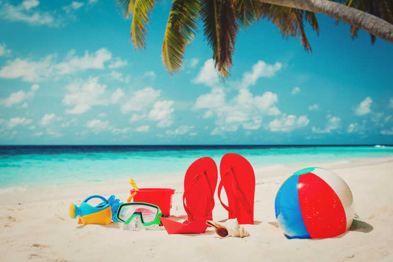 海边的沙滩上有红色拖鞋和各种玩具