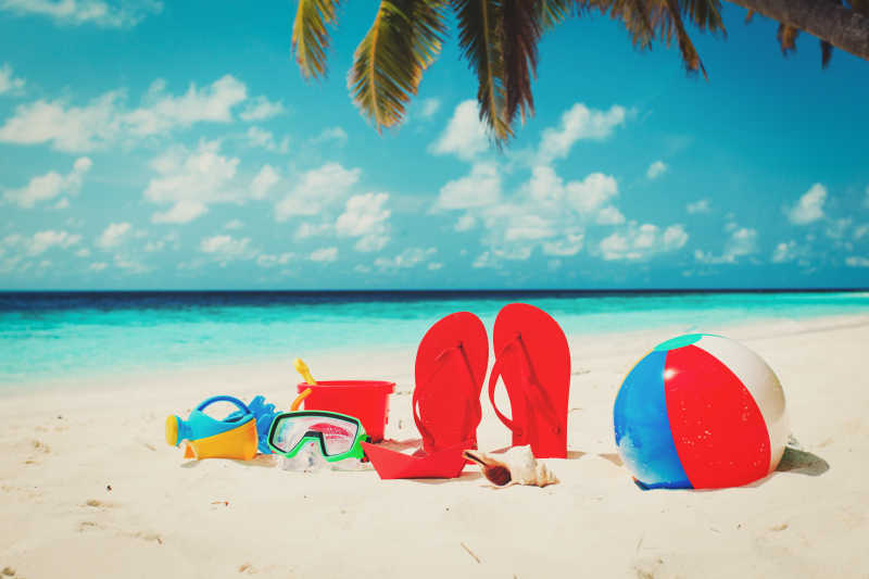 美丽海边的沙滩上放着各种玩具和红色拖鞋