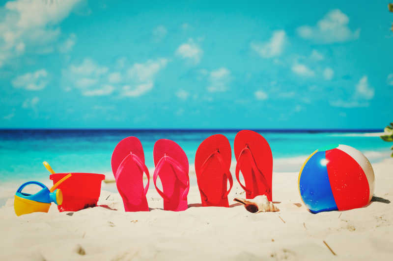 沙滩上的各种玩具和两双红色拖鞋