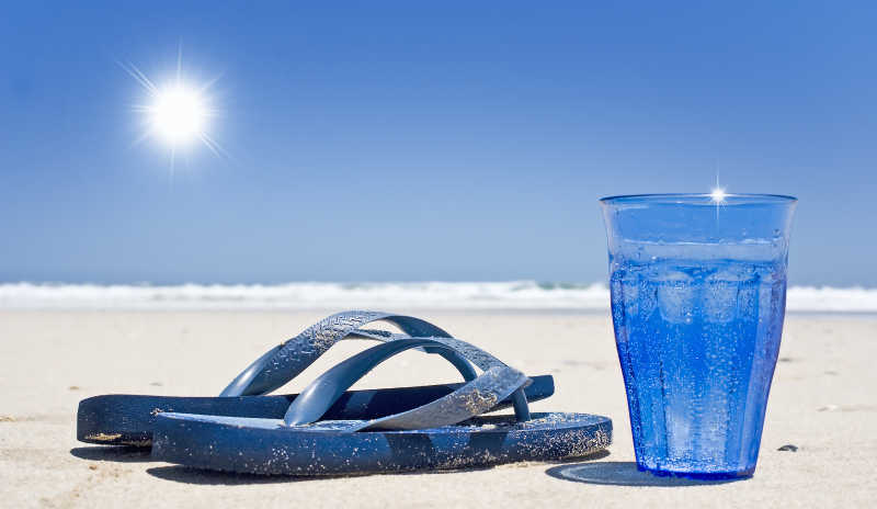 阳光沙滩下的人字拖和一杯水