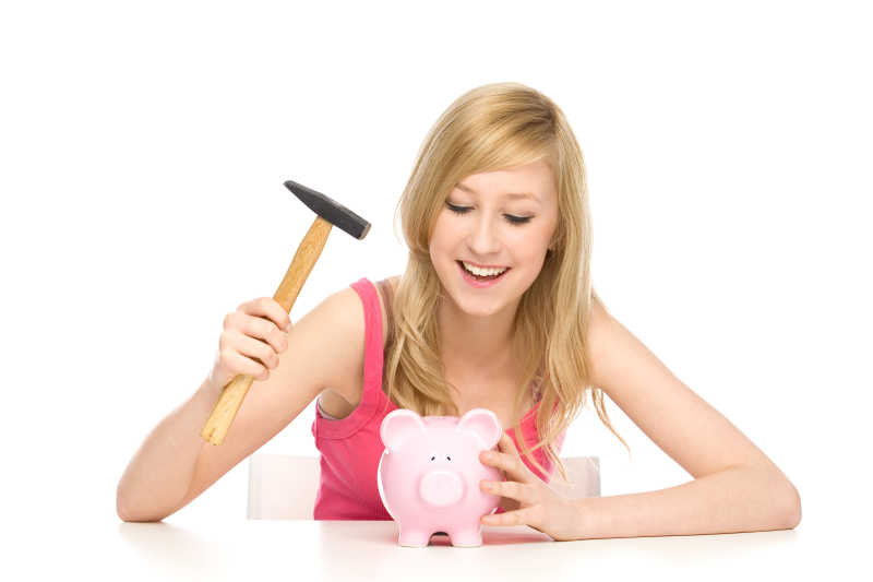 白色背景下拿着锤子砸小猪存钱罐的微笑的女性