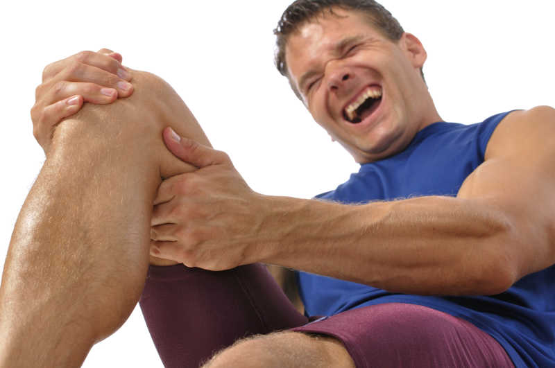 在地板上抓着膝盖和腿筋的男性运动员在白色背景下的极度疼痛