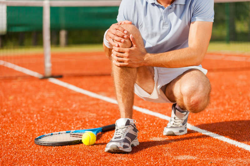 网球运动员坐在网球场上碰到膝盖