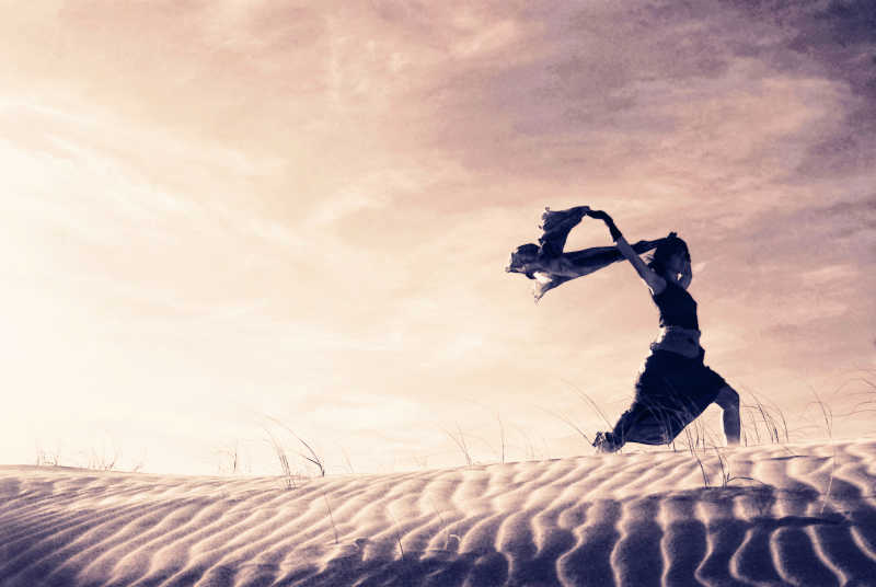 在沙丘上握着围巾奔跑的女人