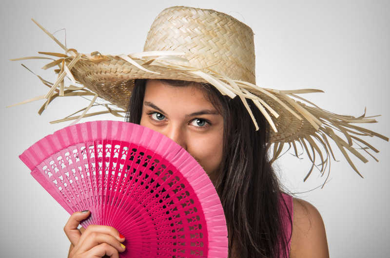 漂亮的年轻女士戴着草帽拿着粉红色的扇子