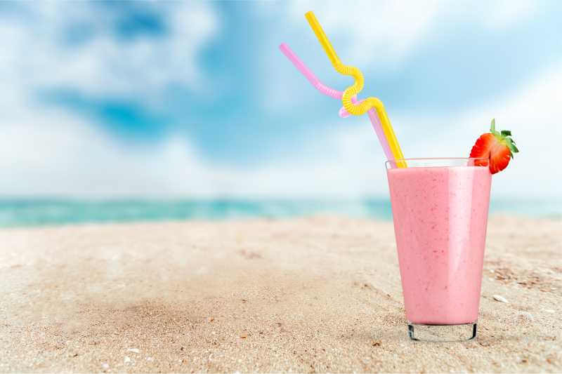 沙滩上一杯粉色的草莓奶昔