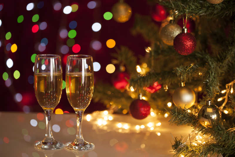 缠绕着五彩小灯的圣诞树旁的两杯香槟酒